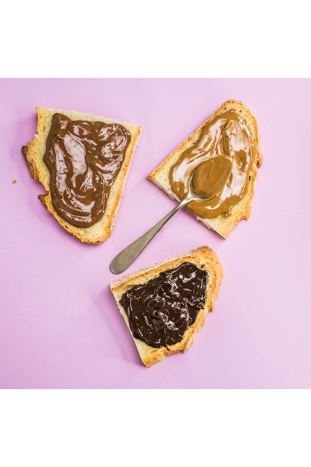 Tre fette di pane con creme di nocciole di diverse tonalità e un cucchiaino, su fondo rosa.