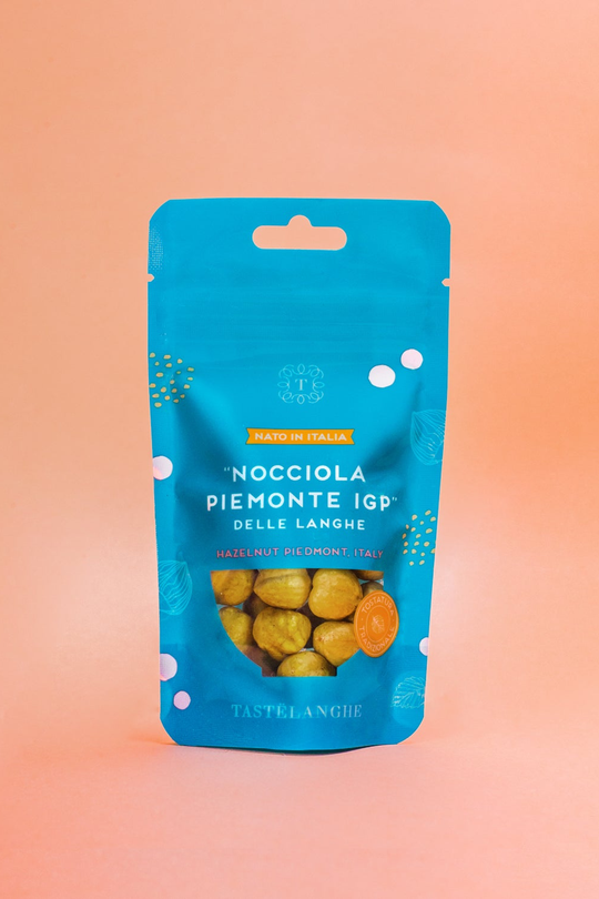 Confezione turchese di Nocciola Piemonte IGP delle Langhe tostata Tastëlanghe, con finestra trasparente, su fondo pesca.