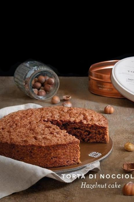 Torta di nocciole Tastëlanghe con una fetta tagliata, latta e nocciole su un tavolo scuro.